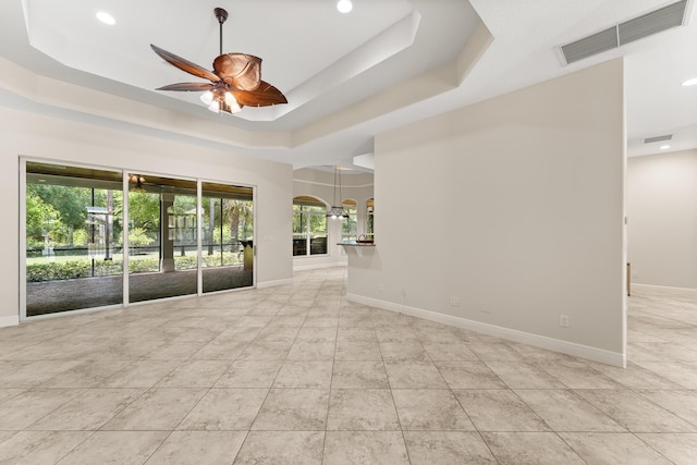 empty room with a ceiling fan, visible vents, tile patterned flooring, and a tray ceiling