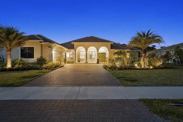 mediterranean / spanish-style home with stucco siding, a tile roof, a front lawn, and decorative driveway