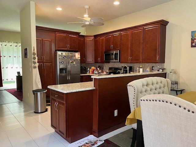 kitchen featuring backsplash, light tile patterned floors, a peninsula, appliances with stainless steel finishes, and ceiling fan