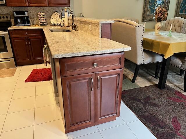 kitchen featuring a sink, stainless steel range with electric cooktop, light tile patterned floors, a peninsula, and light stone countertops