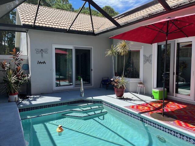 back of house featuring a tile roof, a patio area, glass enclosure, an outdoor pool, and stucco siding