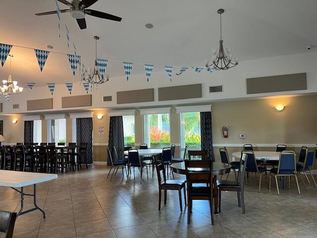 dining area featuring tile patterned flooring, a towering ceiling, visible vents, and ceiling fan with notable chandelier