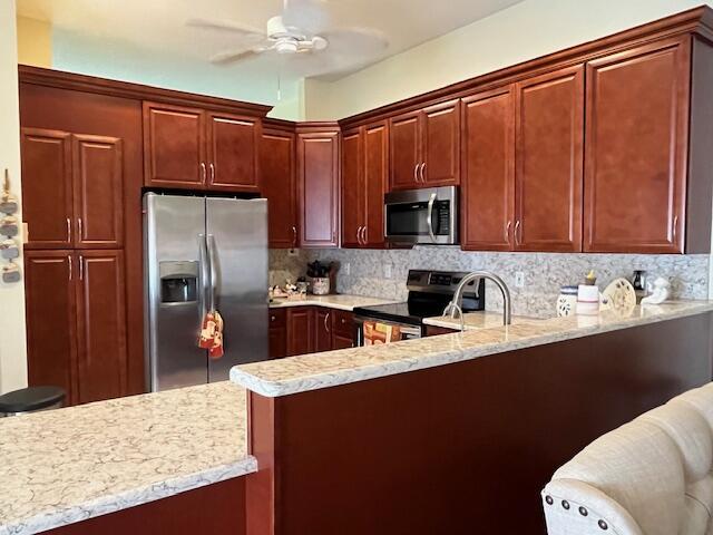 kitchen featuring light stone counters, a peninsula, tasteful backsplash, appliances with stainless steel finishes, and ceiling fan