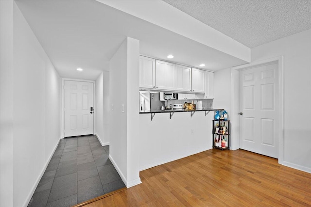 3526 Whitehall Dr Unit 106, West Palm Beach, FL 33401 - kitchen featuring white cabinetry, dark countertops, stainless steel microwave, a breakfast bar area, and refrigerator