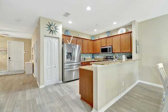 kitchen featuring light wood-style floors, appliances with stainless steel finishes, decorative backsplash, and a peninsula
