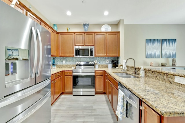 kitchen with appliances with stainless steel finishes, light stone counters, a sink, light wood finished floors, and a peninsula