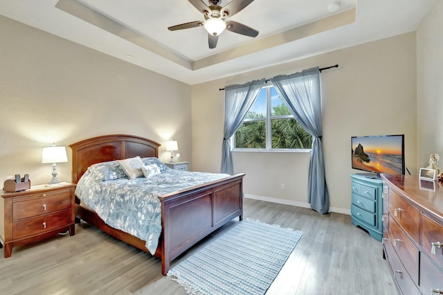 bedroom with light wood-style floors, a raised ceiling, baseboards, and a ceiling fan