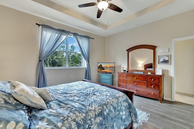 bedroom with light wood-style floors, a raised ceiling, baseboards, and ceiling fan
