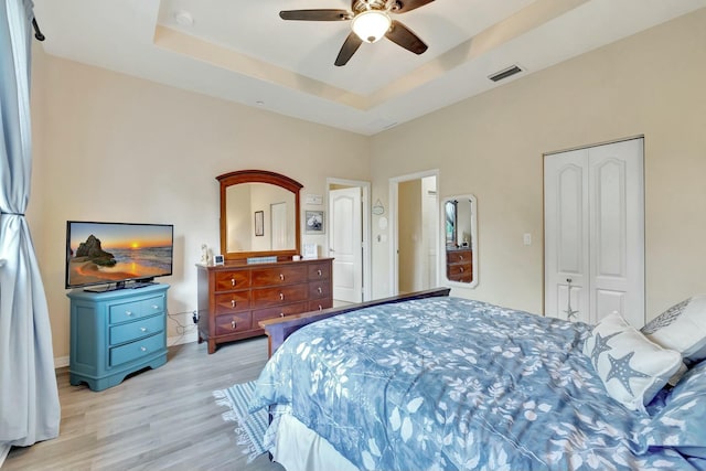 bedroom featuring ceiling fan, a raised ceiling, light wood finished floors, visible vents, and a closet