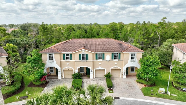 mediterranean / spanish house with a garage, a tiled roof, driveway, and stucco siding