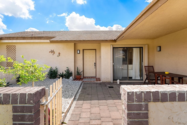 doorway to property featuring a patio, roof with shingles, and stucco siding