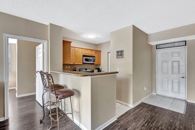 11760 Saint Andrews Pl Unit 204, Wellington, FL 33414 - kitchen with a breakfast bar area, light wood-style flooring, stainless steel microwave, baseboards, and stove