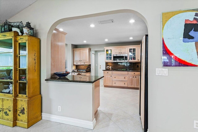kitchen with visible vents, arched walkways, tasteful backsplash, light tile patterned floors, and stainless steel microwave