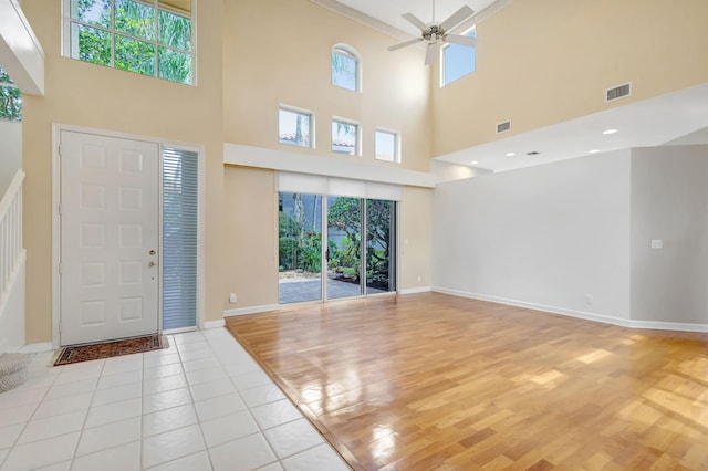 foyer entrance featuring light wood-style flooring, a ceiling fan, visible vents, stairway, and a towering ceiling
