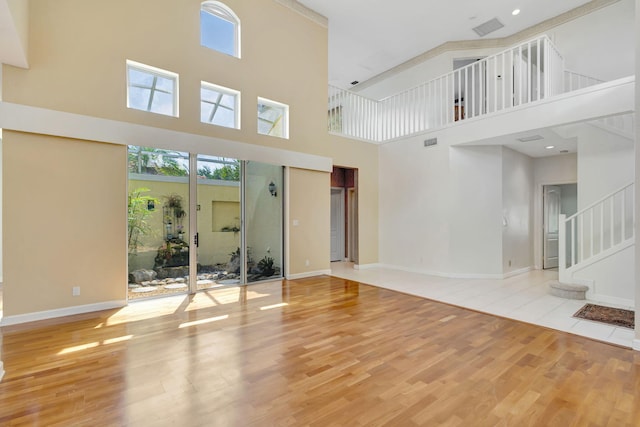 unfurnished living room featuring a healthy amount of sunlight, wood finished floors, baseboards, and a high ceiling