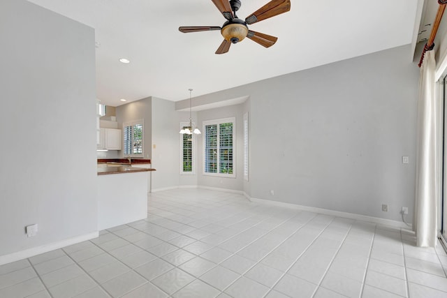 unfurnished living room featuring ceiling fan with notable chandelier, baseboards, light tile patterned floors, and recessed lighting