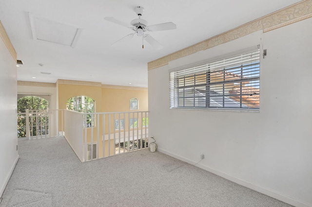 carpeted empty room with baseboards, attic access, and a ceiling fan