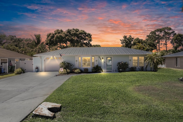 view of front of home with a garage, driveway, metal roof, and a lawn