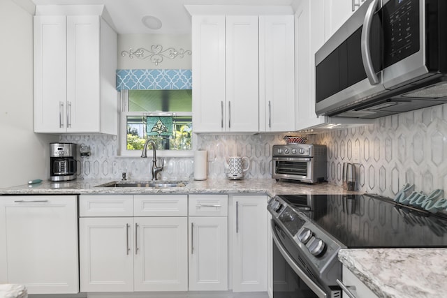kitchen with white cabinets, appliances with stainless steel finishes, decorative backsplash, and a sink