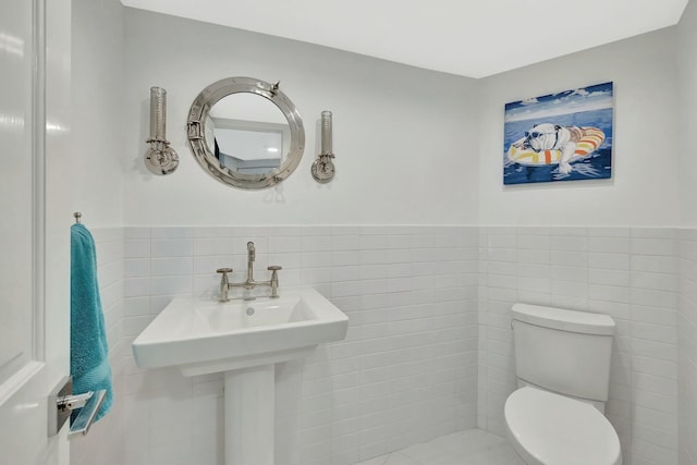 half bathroom featuring toilet, a wainscoted wall, and tile walls