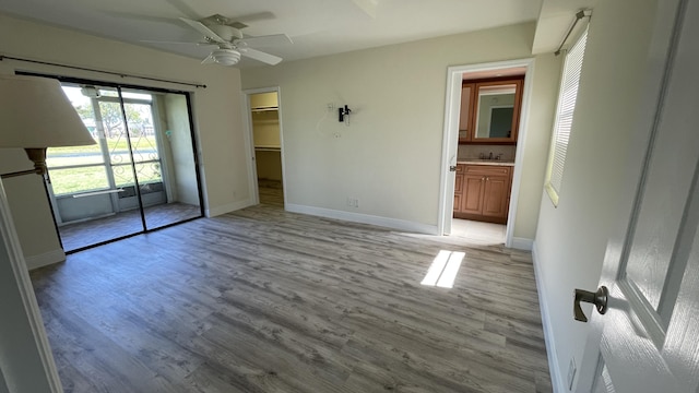 unfurnished bedroom featuring connected bathroom, baseboards, light wood finished floors, a ceiling fan, and a walk in closet