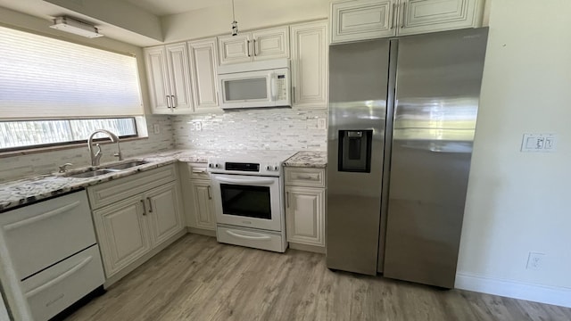 kitchen with a sink, light wood-type flooring, tasteful backsplash, light stone counters, and white appliances