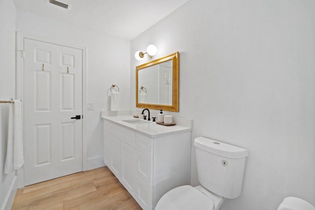 bathroom featuring toilet, vanity, wood finished floors, and visible vents
