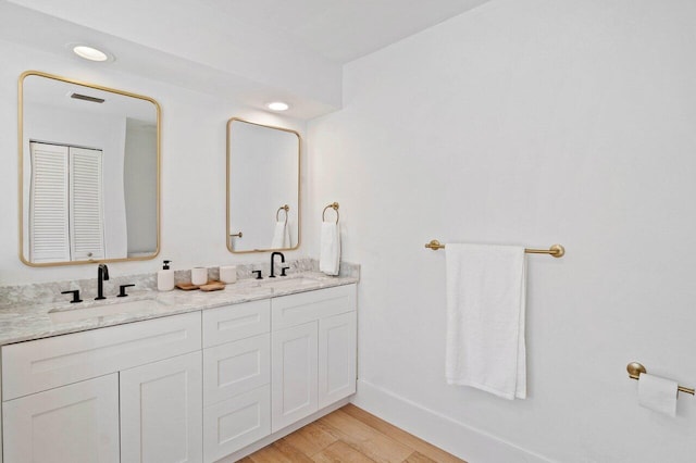 bathroom featuring baseboards, wood finished floors, a sink, and double vanity