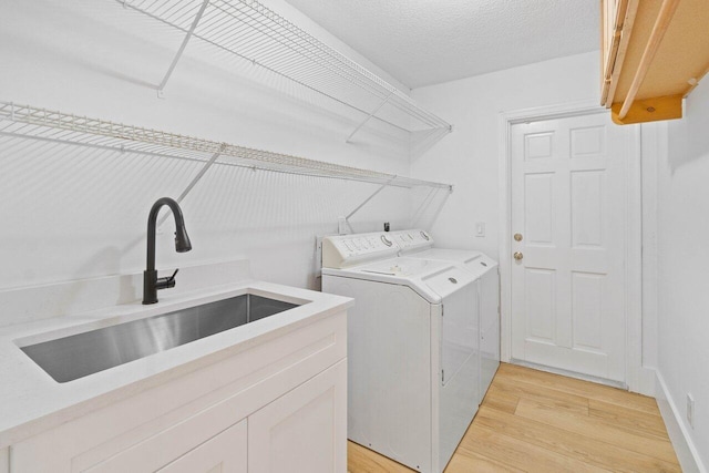 washroom featuring washer and dryer, cabinet space, a sink, and light wood finished floors