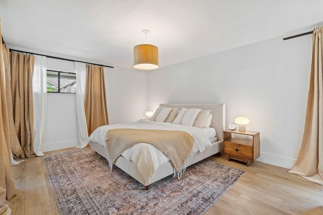 bedroom featuring light wood finished floors, baseboards, and a textured ceiling
