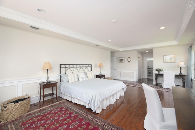 bedroom featuring wood finished floors, a tray ceiling, a decorative wall, wainscoting, and recessed lighting