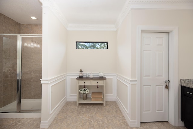 bathroom with a stall shower, a decorative wall, vanity, crown molding, and wainscoting