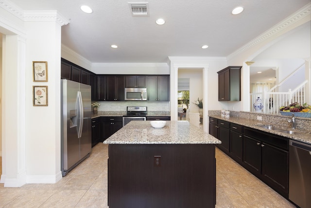 kitchen with stainless steel appliances, a sink, a kitchen island, light tile patterned flooring, and light stone countertops