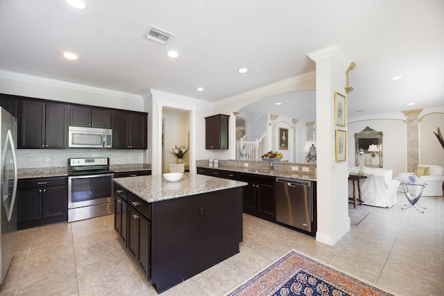 kitchen featuring stainless steel appliances, a center island, decorative columns, decorative backsplash, and light stone countertops