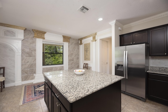 kitchen with stainless steel refrigerator with ice dispenser, light stone countertops, a center island, ornate columns, and ornamental molding
