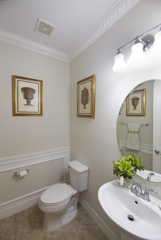half bathroom with a sink, ornamental molding, toilet, baseboards, and tile patterned flooring