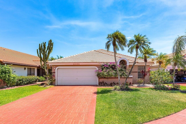 view of front of home featuring a tile roof, decorative driveway, an attached garage, a front yard, and stucco siding