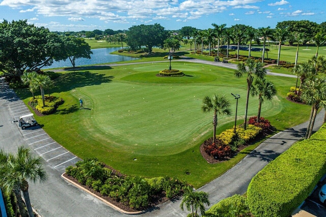 view of community featuring golf course view, a lawn, a water view, and uncovered parking