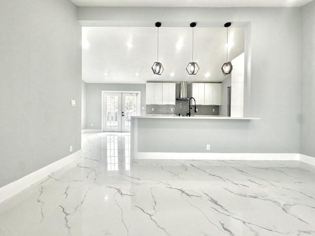 kitchen featuring marble finish floor, french doors, wall chimney exhaust hood, white cabinets, and baseboards