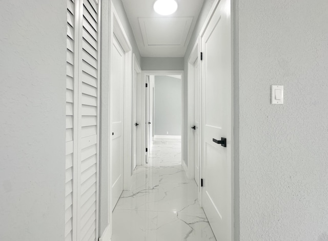 hall featuring a textured wall, marble finish floor, and baseboards