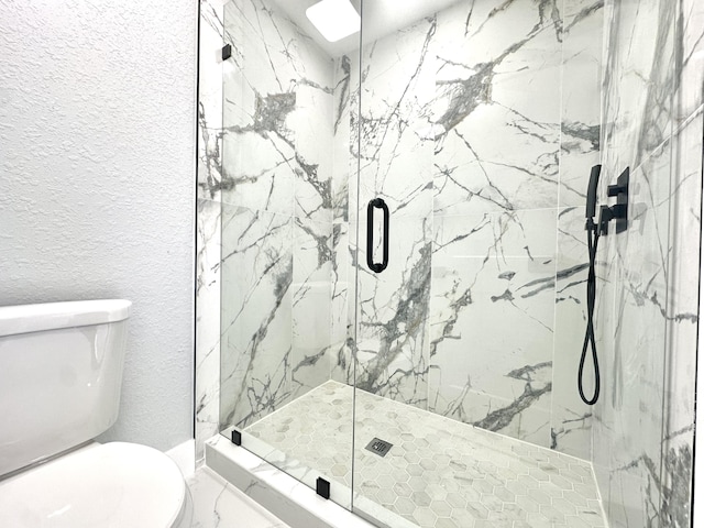bathroom with marble finish floor, toilet, a textured wall, and a marble finish shower