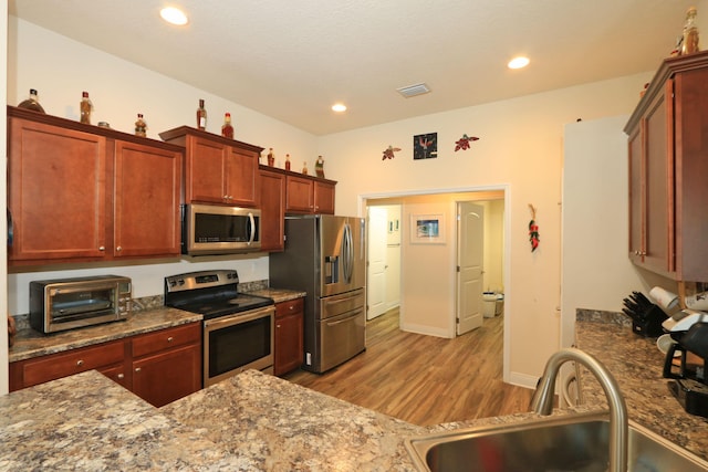 kitchen featuring visible vents, wood finished floors, a toaster, a sink, and stainless steel appliances