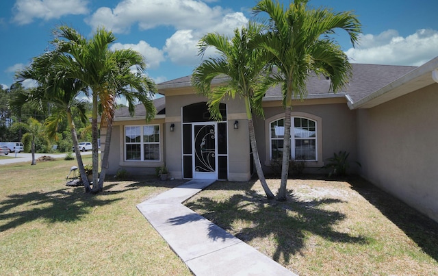 entrance to property with a lawn, a shingled roof, and stucco siding