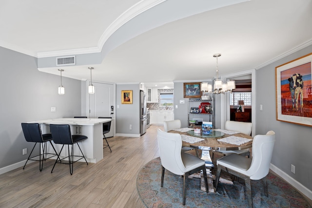 dining room with light wood-type flooring, baseboards, ornamental molding, and an inviting chandelier