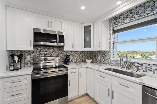 kitchen featuring a sink, decorative backsplash, white cabinetry, appliances with stainless steel finishes, and light stone countertops