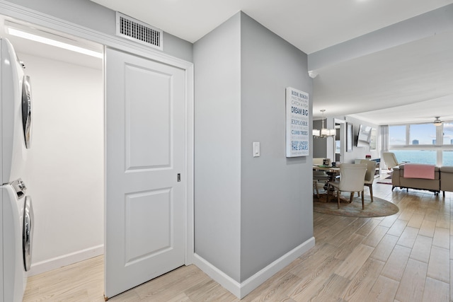 hallway featuring baseboards, stacked washing maching and dryer, visible vents, and light wood-style flooring