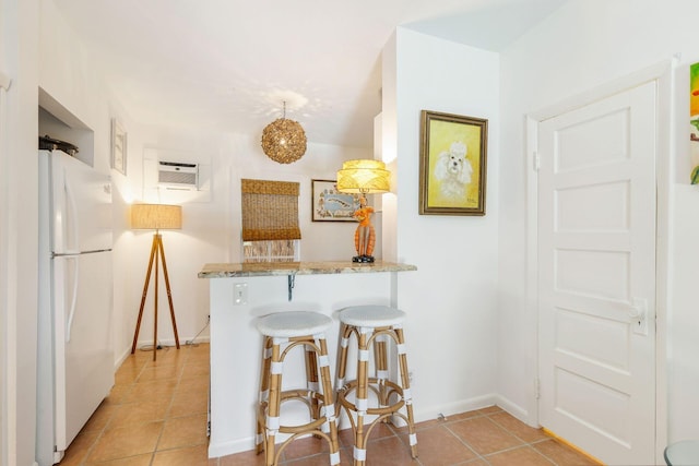 138 Greymon Dr, West Palm Beach, FL 33405 - kitchen with freestanding refrigerator, a peninsula, light tile patterned flooring, a kitchen breakfast bar, and light stone counters