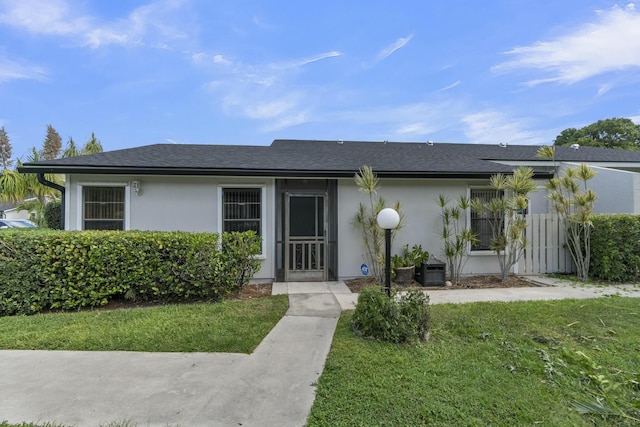 view of front of property featuring a shingled roof, stucco siding, and a front yard