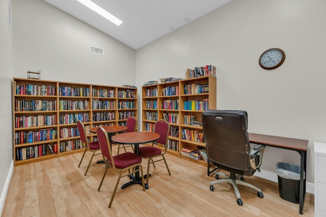 home office with baseboards, visible vents, wood finished floors, and high vaulted ceiling