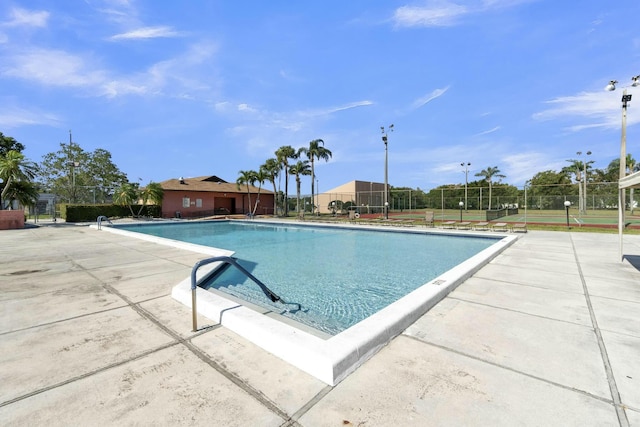 community pool with a patio, a tennis court, and fence